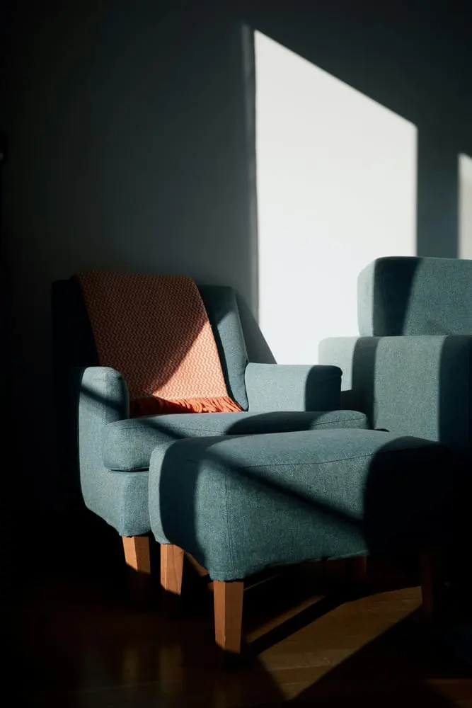an armchair and ottoman with a blanket in sunlight