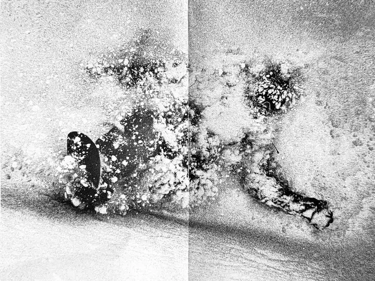 Grainy black and white textured photograph resembling a snowy or sandy surface with dark abstract shapes and holes.